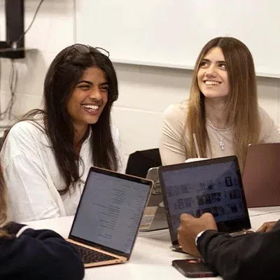 Two female college students sitting at table with laptops and laughing